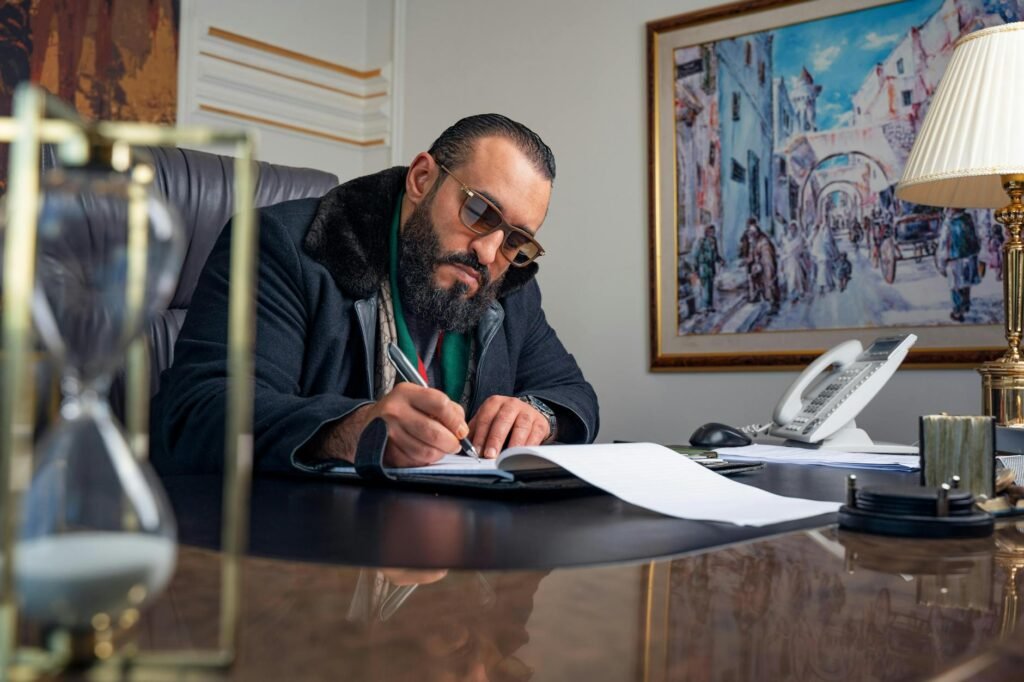 Bearded man with glasses writing at his office desk.